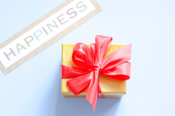 Gift box with red bow with text Happiness on a blue background. Flat lay