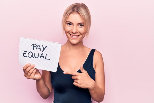 Beautiful blonde woman asking for equality economy holding paper with pay equal message smiling happy pointing with hand and finger