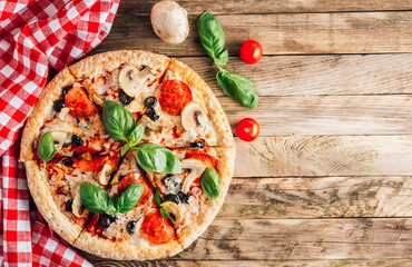 Sliced italian pizza with salami, mozzarella, mushroom, tomatoes, black olives and basil leaves on black background. Italian traditional food. Popular street food concept