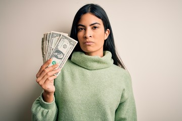 Young beautiful hispanic woman holding a pack of one dollar bunch of dollars with a confident expression on smart face thinking serious