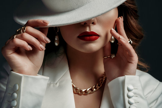 Luxury beautiful fashionable woman wearing stylish accessories: earrings, rings, chain. Hidden eyes with white hat. Female fashion, beauty and advertisement concept. Close up studio portrait