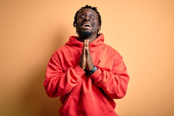 Young african american sporty man wearing sweatshirt with hoodie over yellow background begging and praying with hands together with hope expression on face very emotional and worried. Begging.