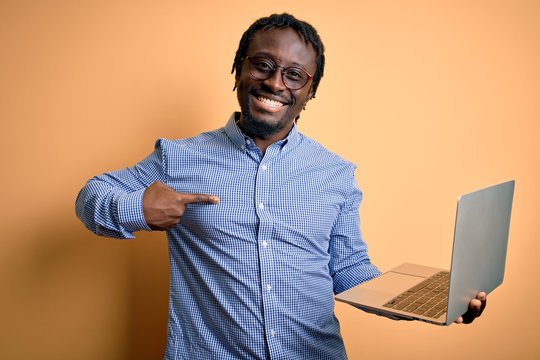 Young african american worker man working using laptop standing over yellow background with surprise face pointing finger to himself