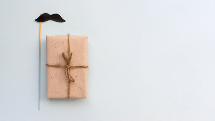 Gift box with kraft paper with a mustache on a light blue background. Flat lay for father's day concept.