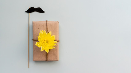 Gift box with kraft paper, flowers and a mustache on a light blue background. Flat lay for father's day concept.