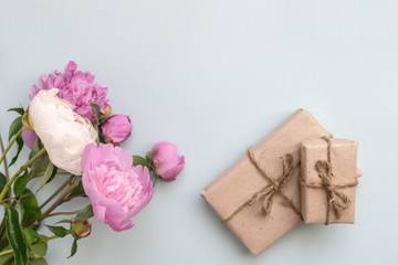 Gift box with kraft paper, peony flowers and a sheet of paper for text on a light blue background. Flat lay for father's day concept.