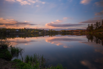 Naklejka na ściany i meble Amazing sunset view of scenic lake near medieval castle on the bank with reflection in the water and reeds on foreground. Svirzh, Ukraine. April 2020