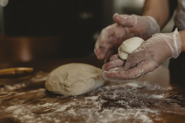 Hands of a woman making dough with plastic gloves on the table