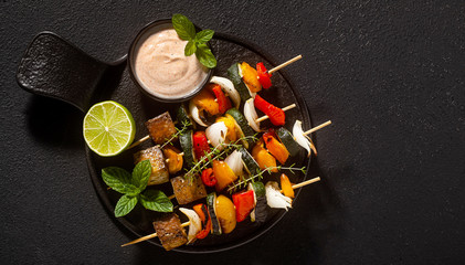 ready vegan kebabs of vegetables and smoked tofu with cashew sauce and smoked paprika on a black...