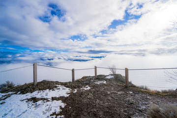 Clouds roll in at the top of the mountain summit with beautiful blue sky's right behind them on Giant head Mountain in Summerland BC