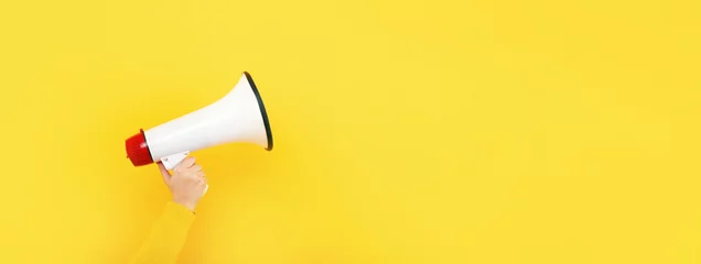 Foto op Canvas megaphone in hand on a yellow background, attention concept announcement, panoramic mock-up © alesmunt