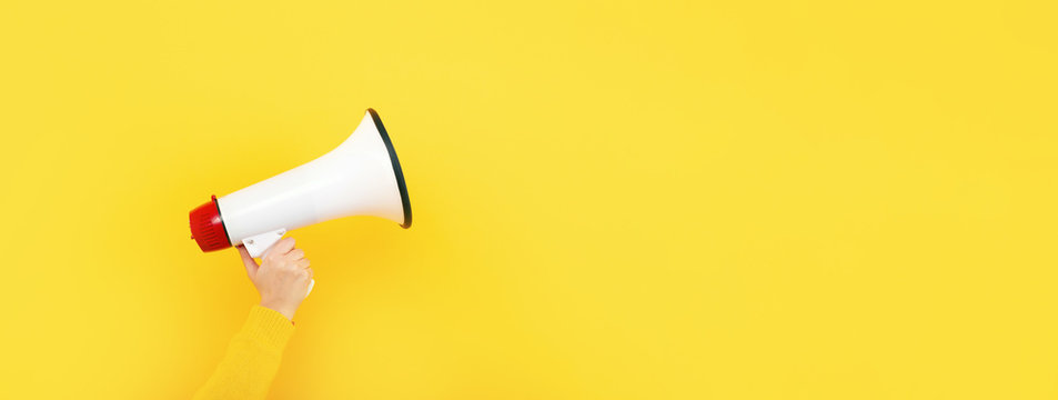 megaphone in hand on a yellow background, attention concept announcement, panoramic mock-up