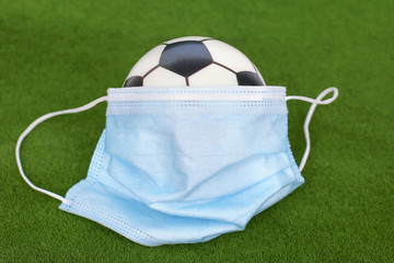 Soccer ball in a medical mask on green background.