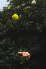 Fliegender Tennisball, welcher in der Luft Wassertropfen von sich weist.