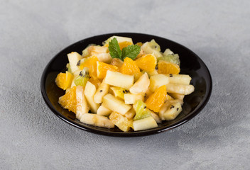 Fruit salad of kiwi, banana, Apple and orange on a plate on a light gray background 