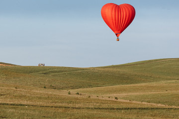 Hot air balloon in shape of heart is landing on the green field