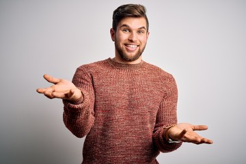 Young blond man with beard and blue eyes wearing casual sweater over white background smiling cheerful with open arms as friendly welcome, positive and confident greetings