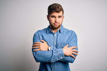 Young handsome blond man with beard and blue eyes wearing casual denim shirt shaking and freezing for winter cold with sad and shock expression on face