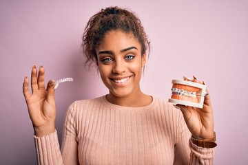 Young african american woman smiling happy holding professional orthodontic denture with metal...