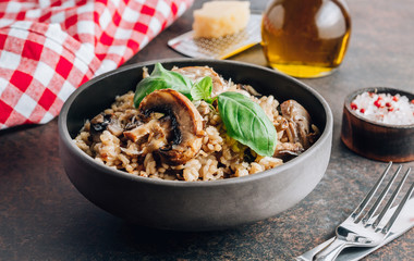 Traditional italian risotto with mushrooms and parmesan cheese on a dark bowl on a black table.