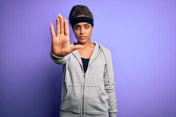 Young african american sportswoman doing sport wearing sportswear over purple background doing stop...