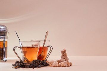 Hot aromatic tea on pink background. Glass teapot. Stack of brown sugar and infusion. Copy space. Tea ceremony concept