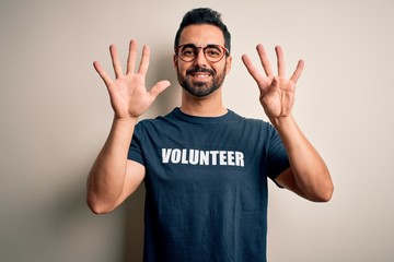 Handsome man with beard wearing t-shirt with volunteer message over white background showing and pointing up with fingers number nine while smiling confident and happy.