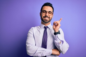Handsome businessman with beard wearing casual tie and glasses over purple background with a big smile on face, pointing with hand and finger to the side looking at the camera.