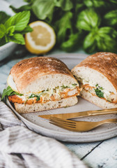 Breakfast table with fresh fried fish sandwich with tartare sauce, lemon and arugula cut in halves, fresh greens on plate over rustic wooden table. Healthy easy breakfast ideas