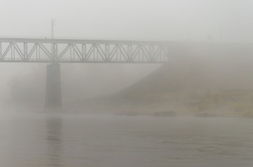 Autumn landscape. Strong fog over the river. Bad visibility. Danger on the sea route. Railway bridge in the distance. Terrible autumn weather.