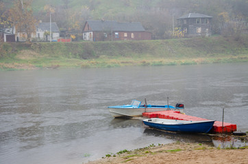 Sad autumn landscape. Fog and rain over the river. Rescue boats stand at the shore. Walk on the...