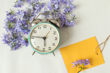 Greeting card-wishes of good mood and good morning . Alarm clock with blue flowers and a place for writing, top view
