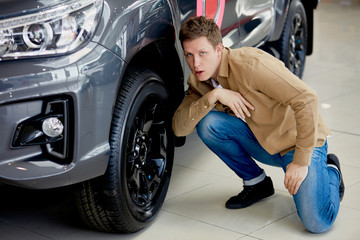 Fototapeta na wymiar Handsome young man in casual wear checking wheels in a new car, surprised with it's perfection