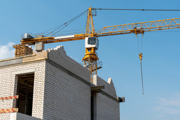 Orange tower crane against a clear blue sky. Construction of a new brick building. Modern construction site. Housing on credit, mortgages, sale of real estate.