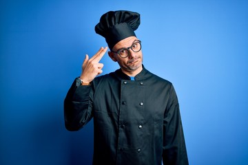 Young handsome chef man wearing cooker uniform and hat over isolated blue background Shooting and killing oneself pointing hand and fingers to head like gun, suicide gesture.