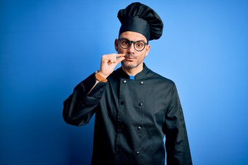Young handsome chef man wearing cooker uniform and hat over isolated blue background mouth and lips shut as zip with fingers. Secret and silent, taboo talking
