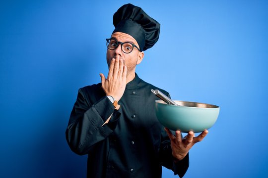 Young handsome chef man wearing cooker uniform and hat mixing using whisk and bowl cover mouth with hand shocked with shame for mistake, expression of fear, scared in silence, secret concept