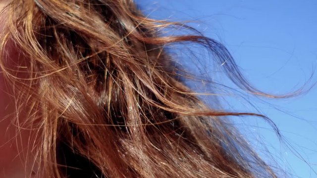 Close up side view of curly brown hair blows in the wind in slow motion. Half face of young caucasian woman and auburn hairs blowing in the air.