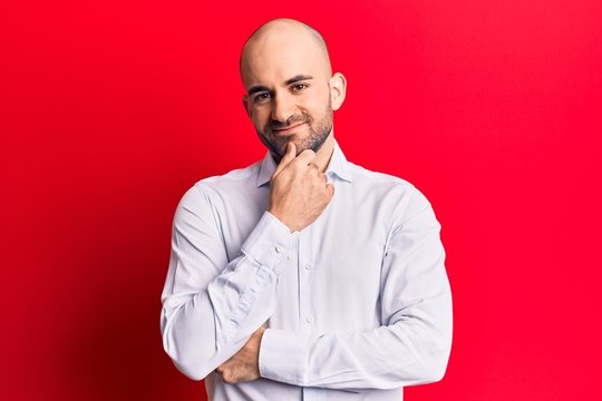 Young handsome bald man wearing elegant shirt smiling looking confident at the camera with crossed arms and hand on chin. thinking positive.