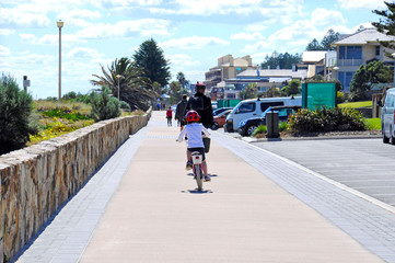 Mother and daughter child on bicycles cycling along the Esplanade walkway. Taken at Grange, Henley Beach, South Australia, with negative copy space.