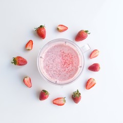 Vista desde arriba de un jugo de frezas rodeado por frutas de frezas en una mesa blanca.