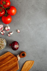 Vegetables, tomatoes, garlic, onions, mint, spices on cement table with blank of wooden kitchen board, top view. Rustic style. Flat lay