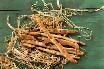 Breadsticks grissini with raisins on a green wood background.