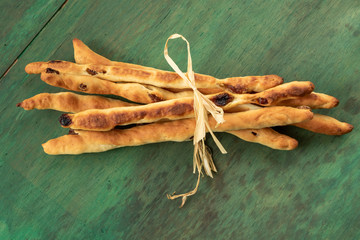Breadsticks grissini with raisins on a green wood background.