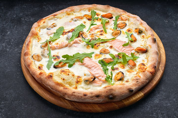 Seafood pizza, marinara, di mare, with salmon, mussels and arugula, on a wooden board, against a dark background