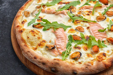 Seafood pizza, marinara, di mare, with salmon, mussels and arugula, on a wooden board, against a dark background
