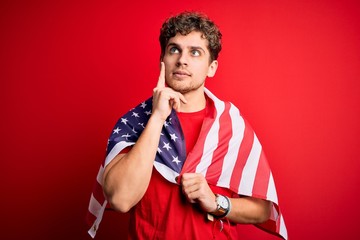 Young blond patriotic man with curly hair wearing USA flag celebrating independence day serious...