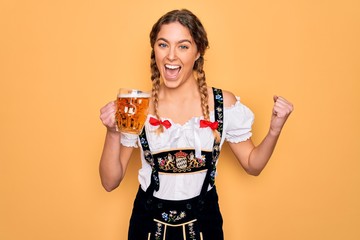 Beautiful blonde german woman with blue eyes wearing octoberfest dress drinking jar of beer screaming proud and celebrating victory and success very excited, cheering emotion