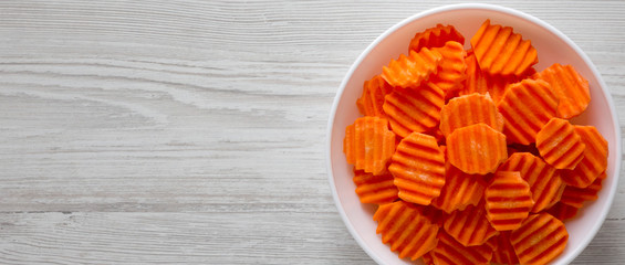Fresh Raw Organic Carrot Chips in a white bowl on a white wooden surface, top view. From above, overhead, flat lay. Space for text.