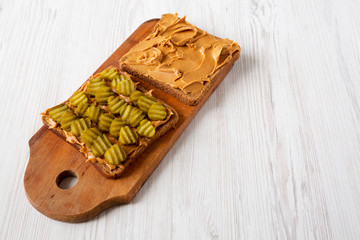 Homemade Peanut Butter Pickle Sandwich on a rustic wooden board on a white wooden background, low angle view. 